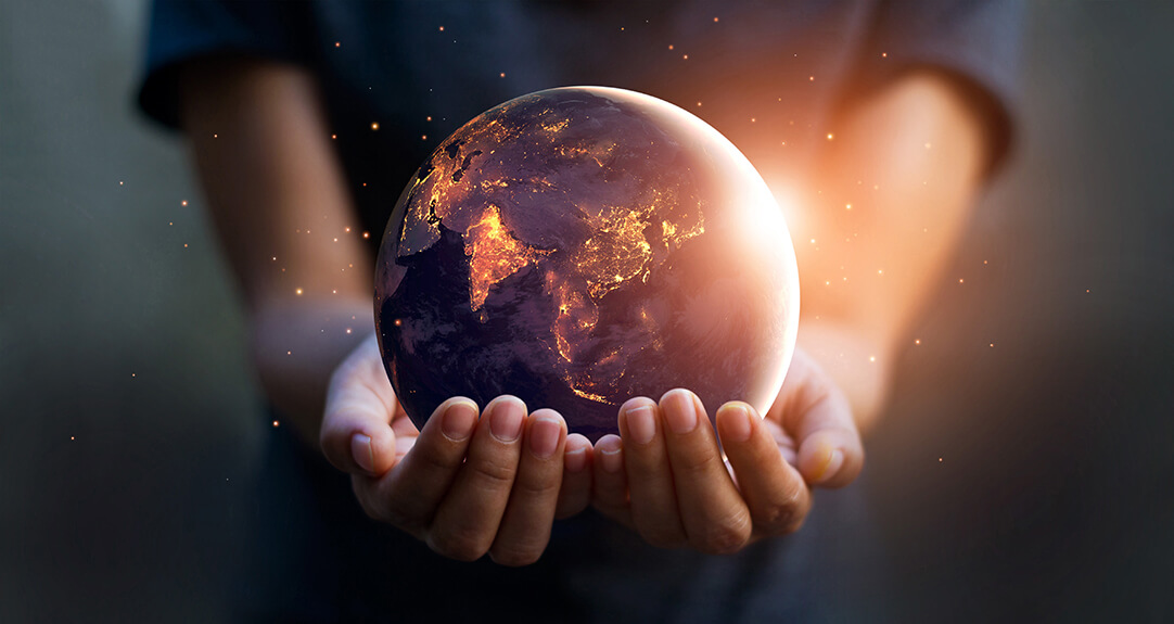 A person holds a glowing, translucent globe in their hands, showing a brightly illuminated map of the world with continents highlighted in warm colors.