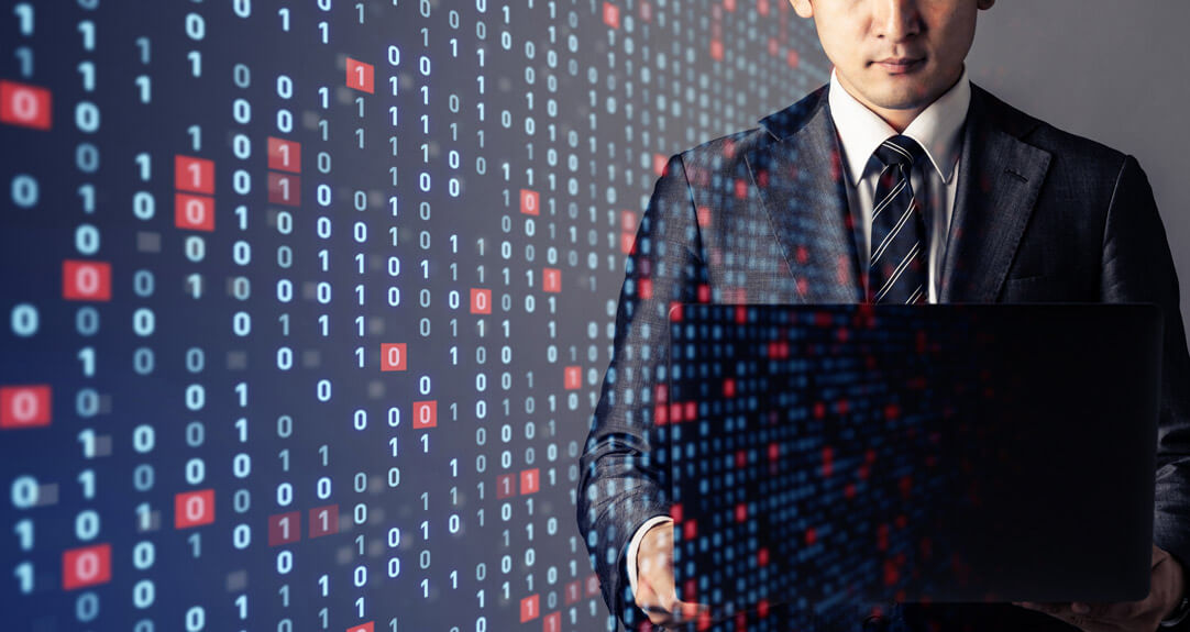 A businessman in a suit stands confidently while working on a laptop, with a background of binary code (0s and 1s) projected around him, representing actuaries working with AI.