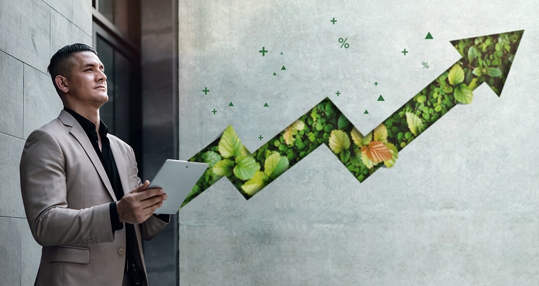 A business professional man in a beige suit holds a tablet while looking thoughtfully to the side. Behind him, a large upward-pointing arrow made of green leaves and foliage symbolizes ESG principles.