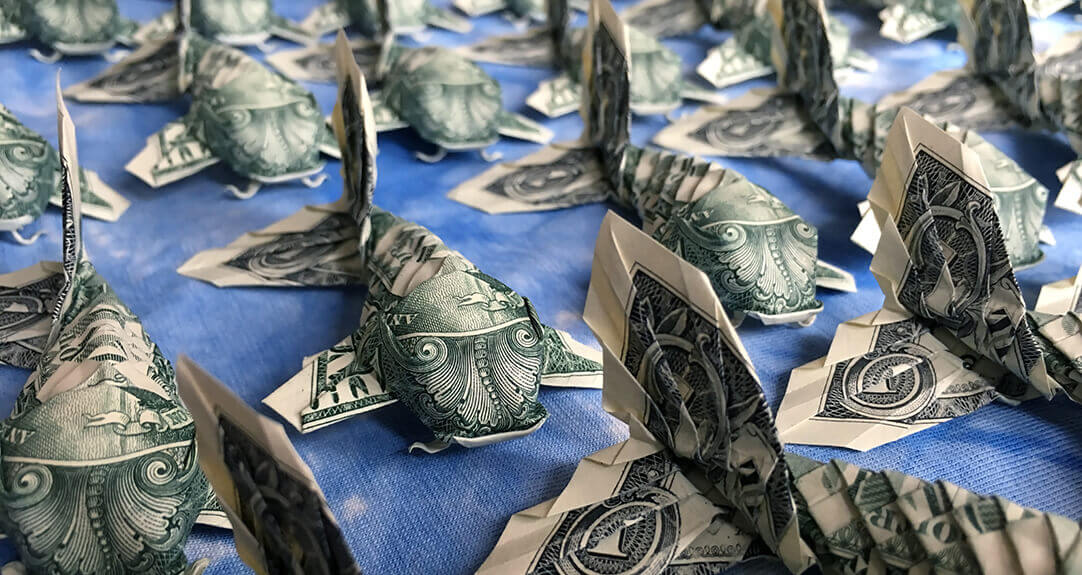 An intricate arrangement of origami koi fish, folded from real one-dollar bills, spread across a blue background.